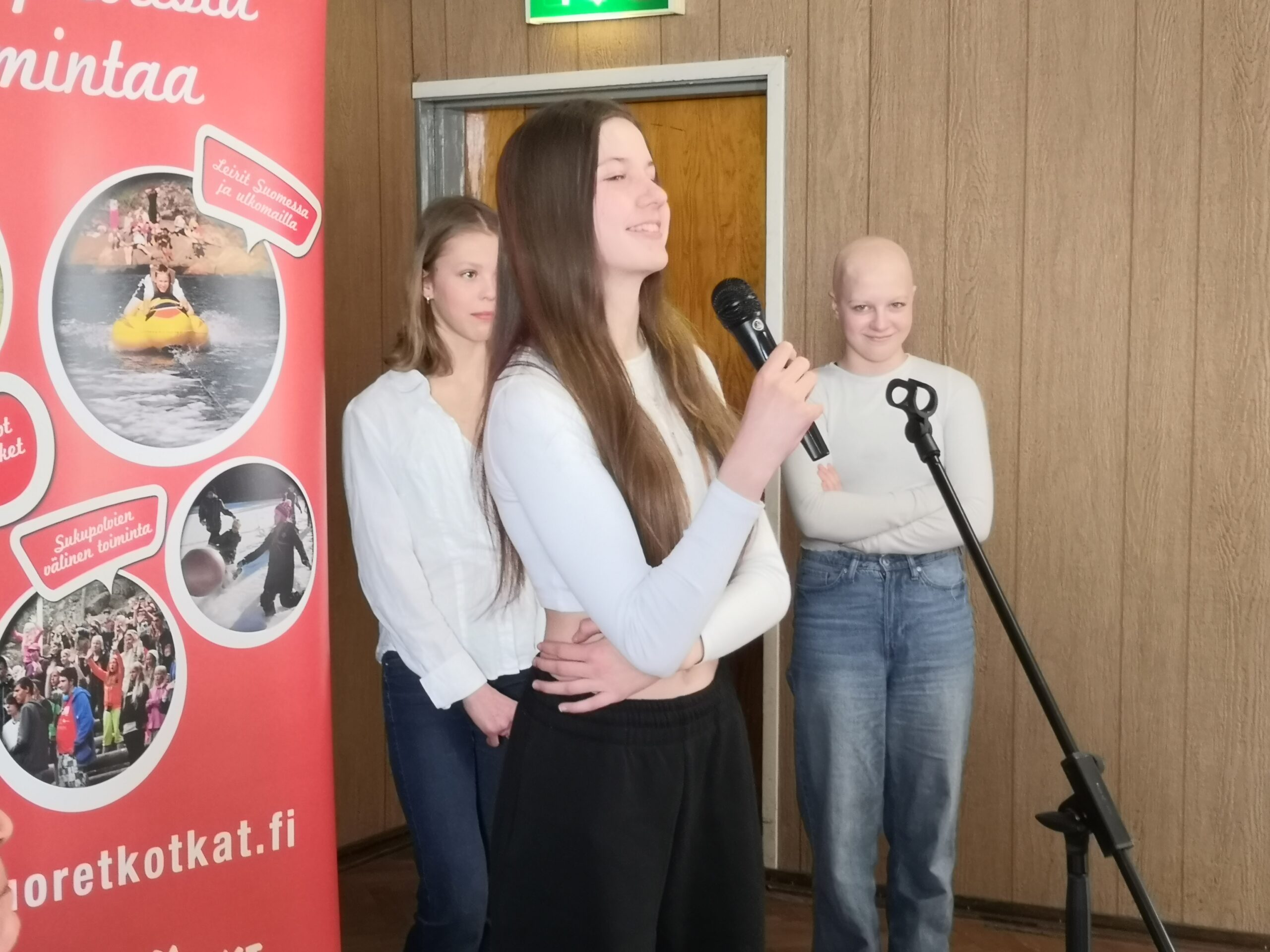 Kolme nuorta pitää puhetta mikrofonin ääressä Nuorten Kotkien rollupin edessä