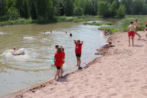 Lapsia punaisissa paidoissa kesäisenä päivänä uimassa kosteikolla. 